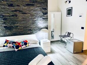 A modern bedroom with a stone wall, a bed with colorful pillows, a white nightstand, a desk with a chair, and a wardrobe. - Franz Guest House (Naples)