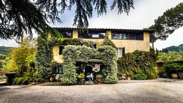 Una casa de dos plantas con fachada de piedra, muros cubiertos de hiedra y un pequeño patio con mesa y sillas.