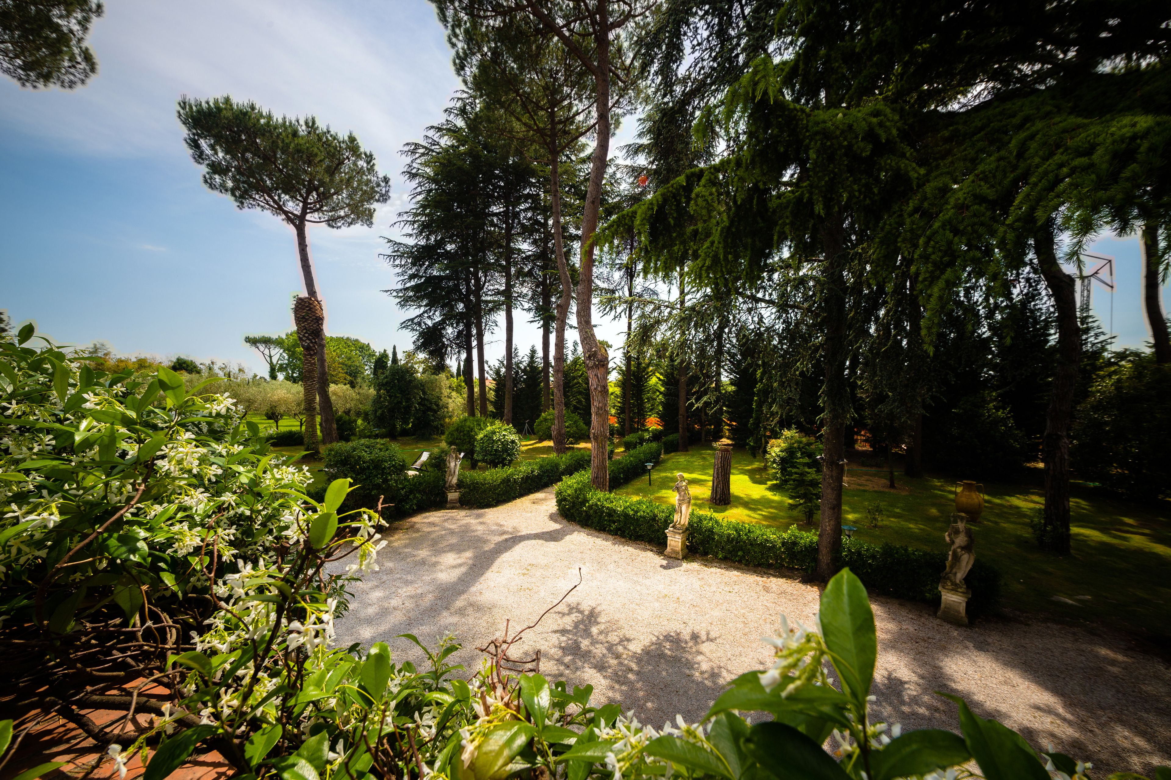A garden with a gravel path, neatly trimmed hedges, and statues.