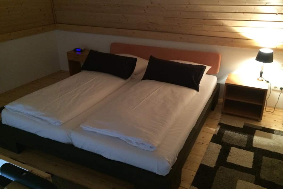 A double bed with two pillows, a nightstand with a lamp, and a wooden headboard.