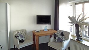 A small, well-lit room with a wooden table and two chairs, a flat-screen TV mounted on the wall, and a radiator. - Hotel Stadt Coblenz (Fachbach)