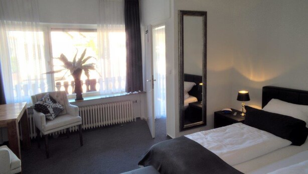 A hotel room with a large bed, a desk with a chair, a small table, a mirror, and a potted plant. - Hotel Stadt Coblenz (Fachbach)
