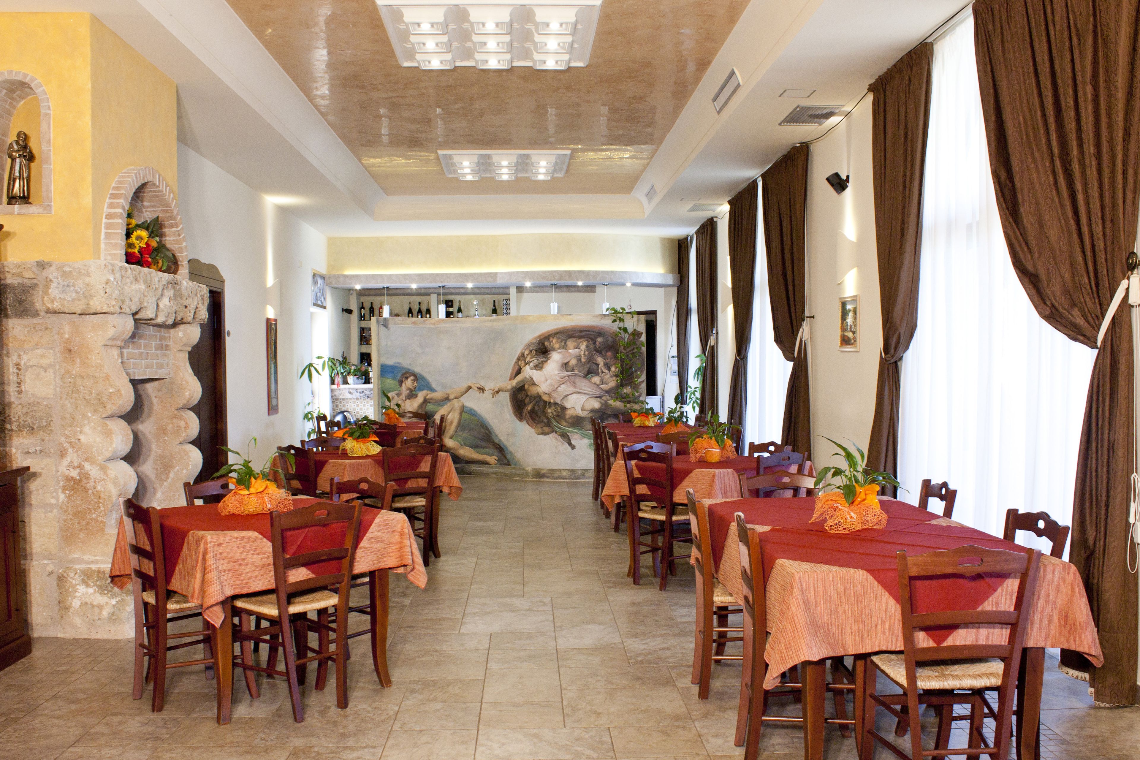 A dining area with multiple tables and chairs, a stone wall with a mural, and a large window with curtains.