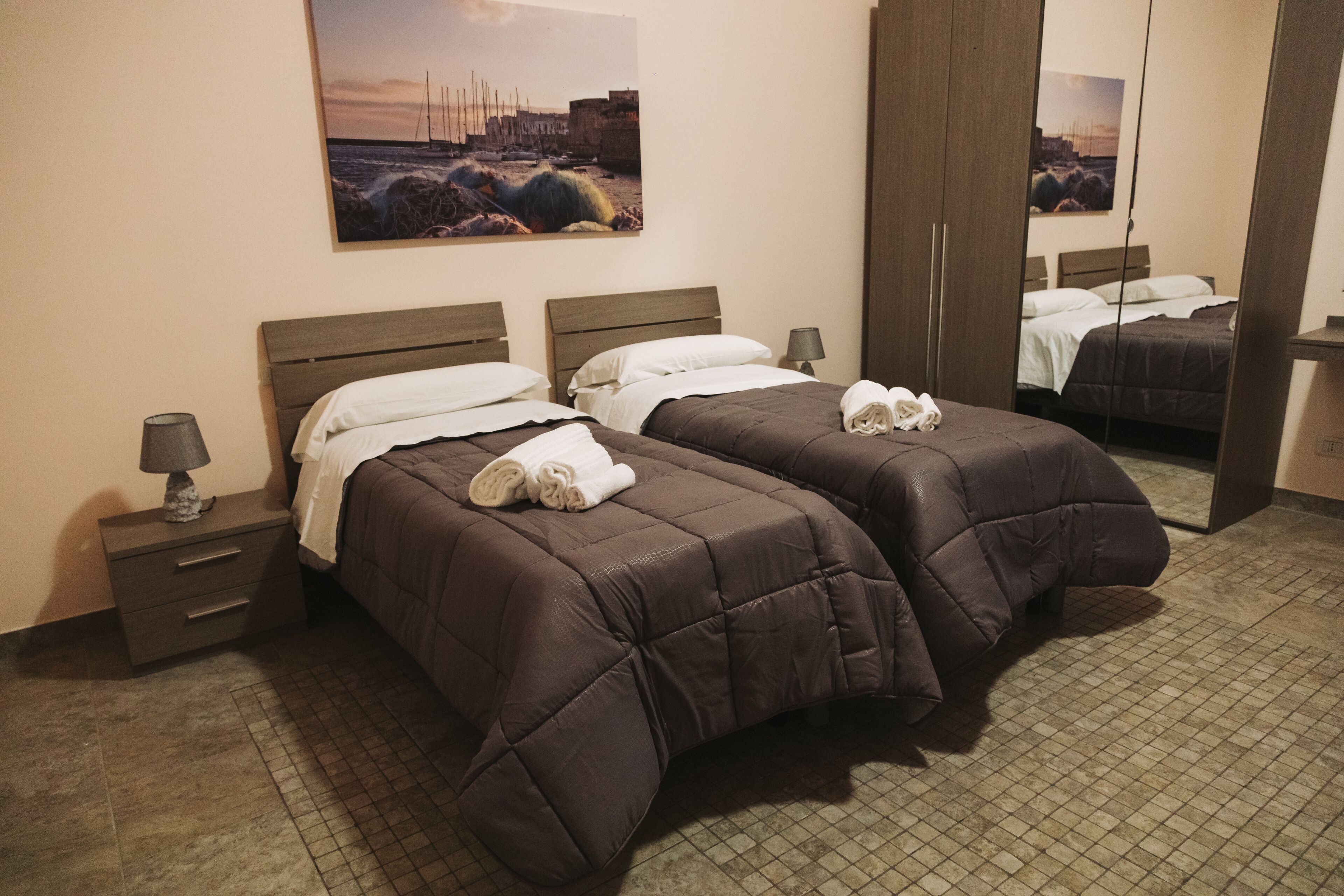 Una habitación de hotel con dos camas, una mesita de noche, una lámpara y un cuadro en la pared.