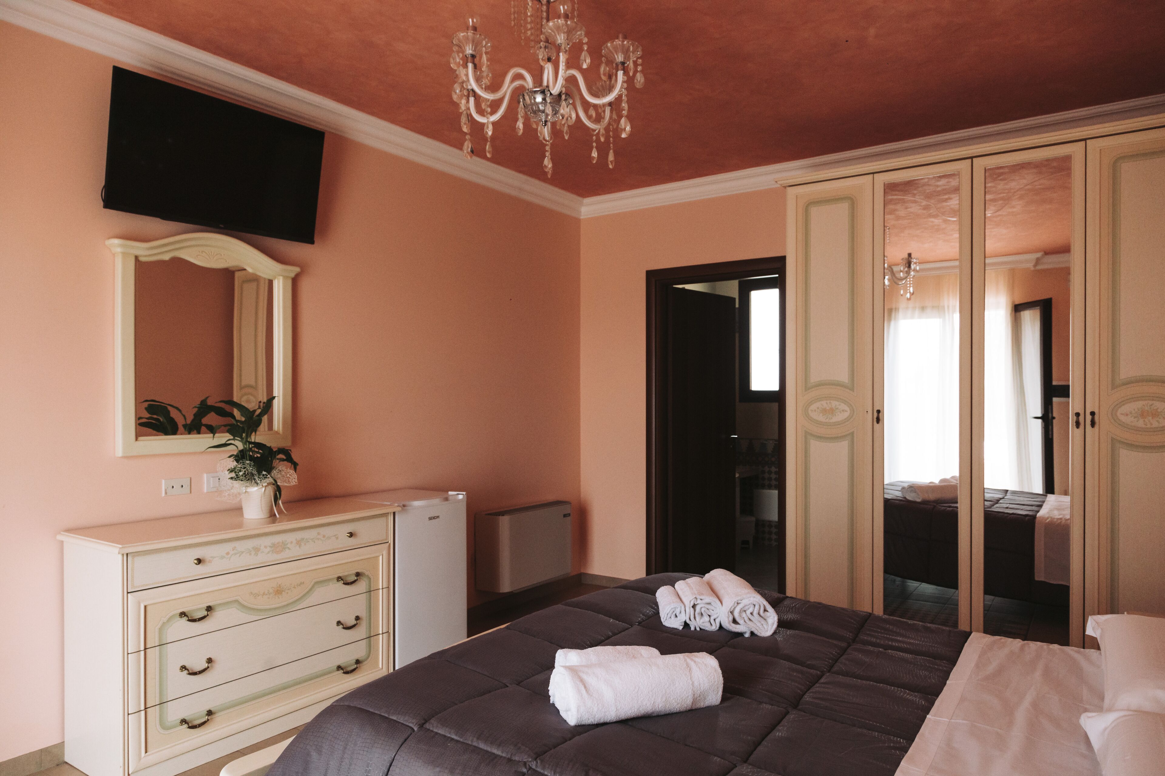 Une chambre à coucher avec un lit, une commode, un miroir et un téléviseur fixé au mur.