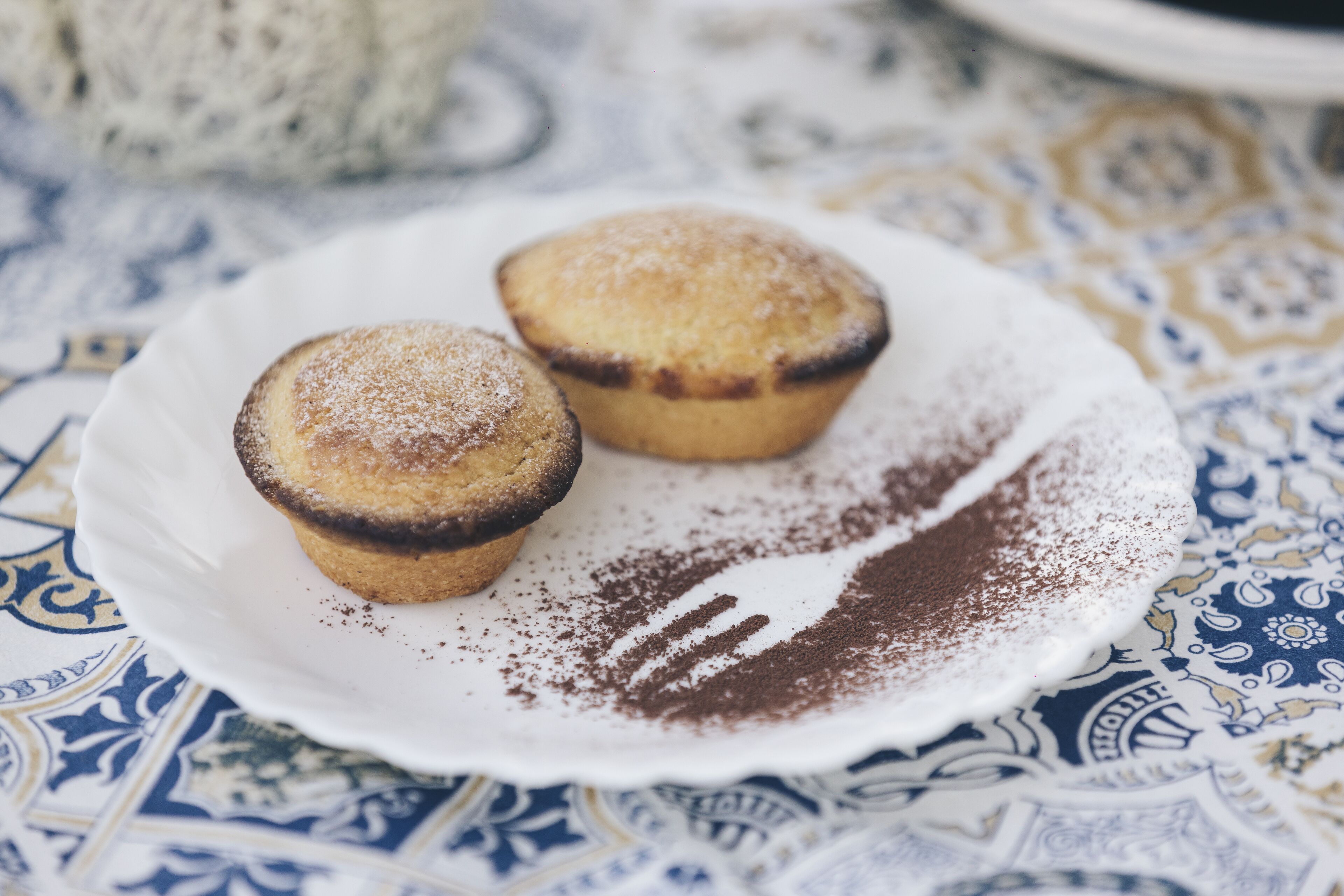A plate with two muffins on a patterned tablecloth.
