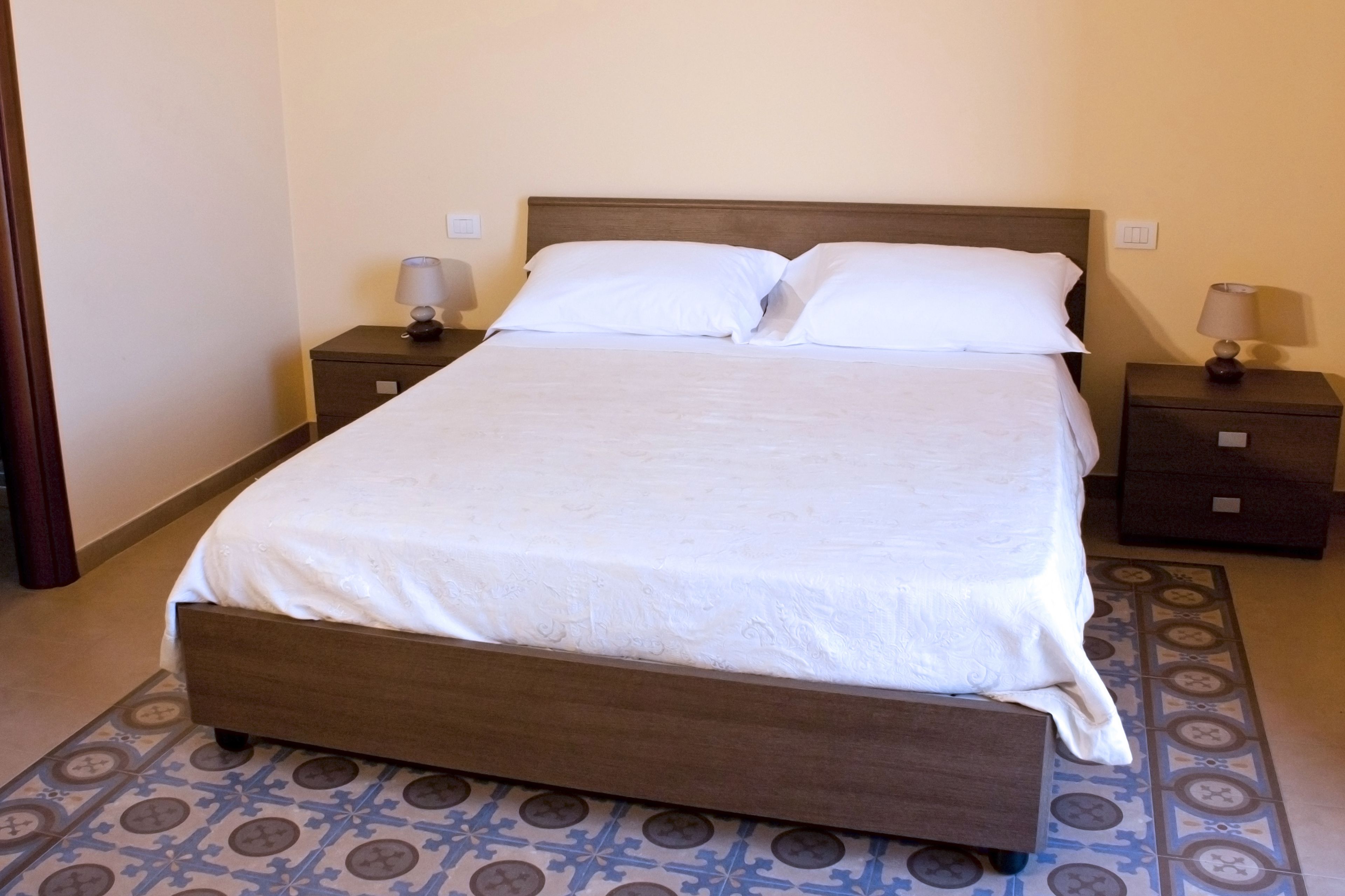 A neatly made bed with a wooden headboard, two bedside tables with lamps, and a patterned floor.