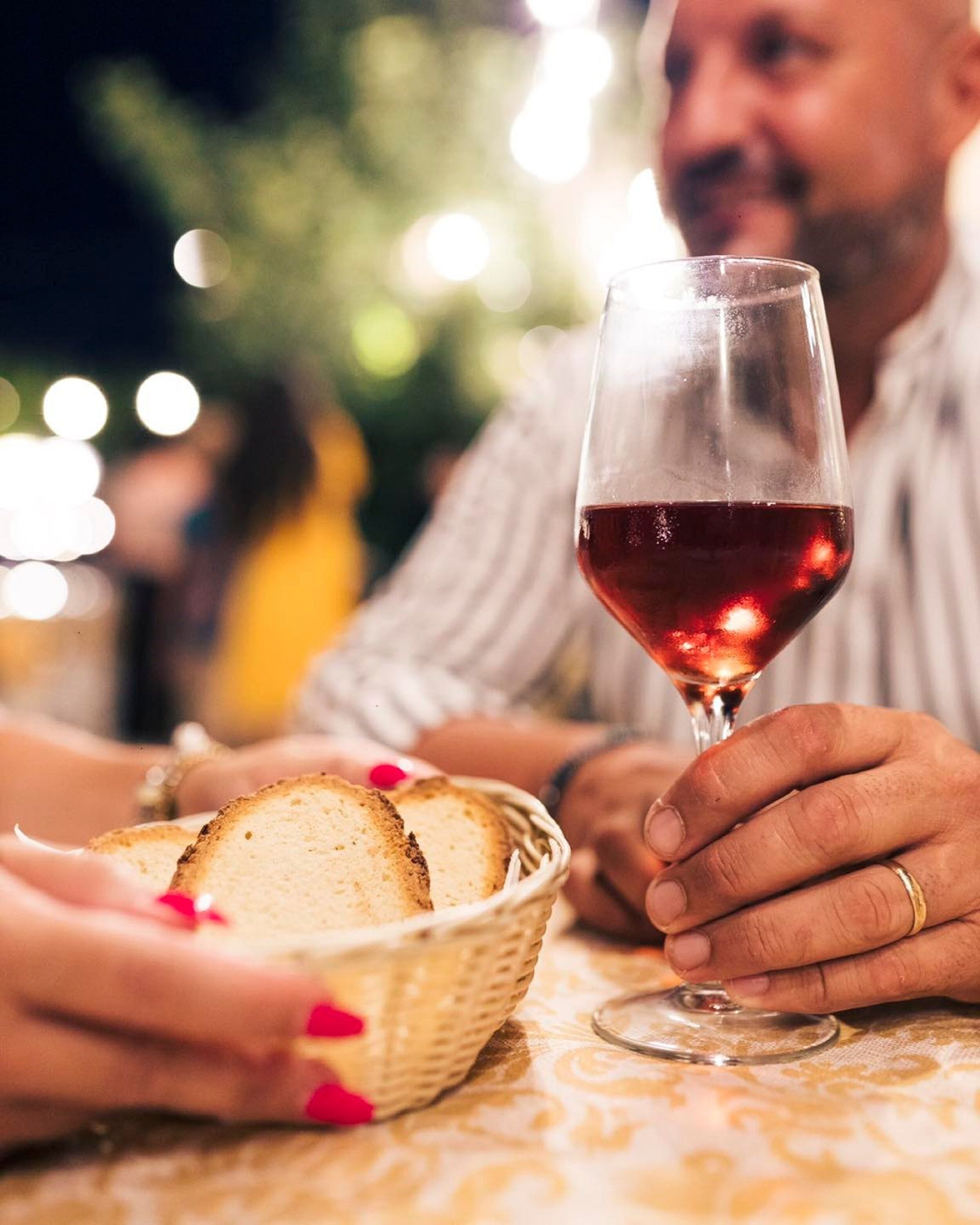 A dining table with a glass of red wine and a basket of bread.