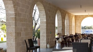 An outdoor patio with stone arches, wicker furniture, and a statue. - Agriturismo Paradiso (Parabita)