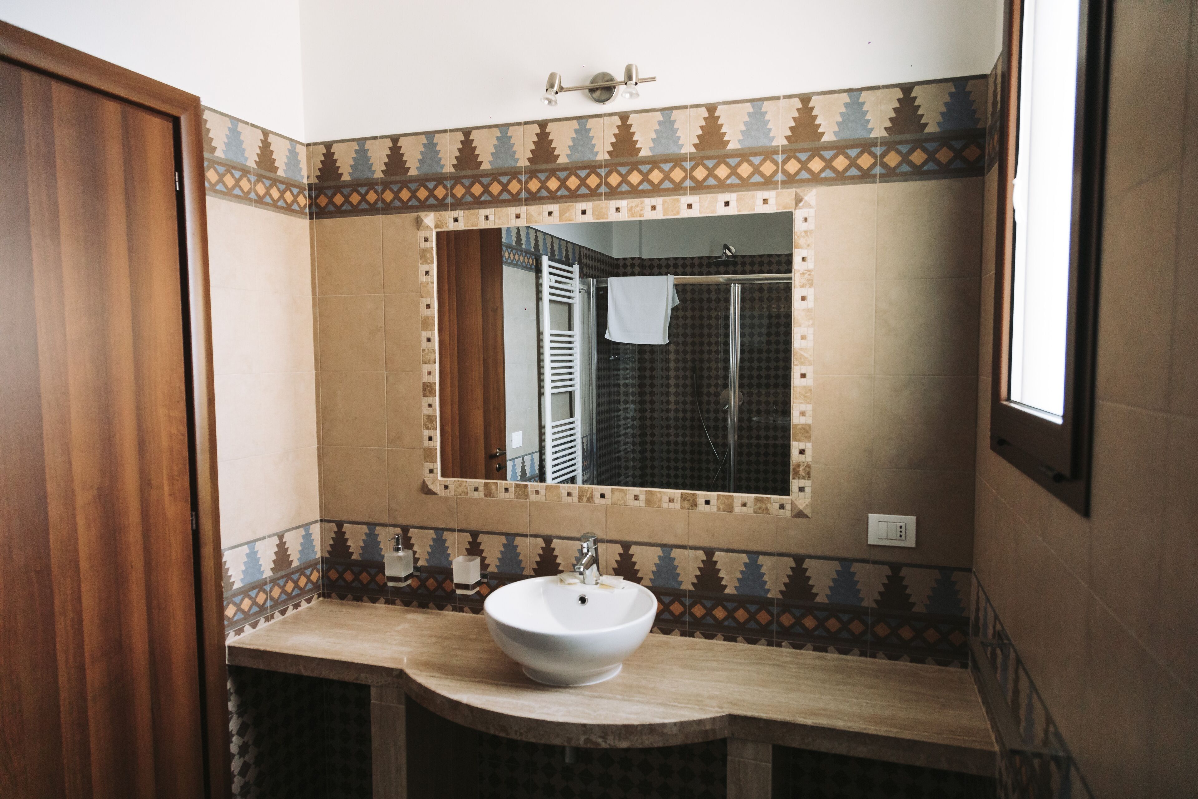 A bathroom with a white sink, a mirror, and patterned tile walls.