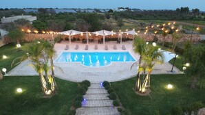 A pool area with a stone pathway leading to the pool, surrounded by lounge chairs and string lights. - Agriturismo Paradiso (Parabita)