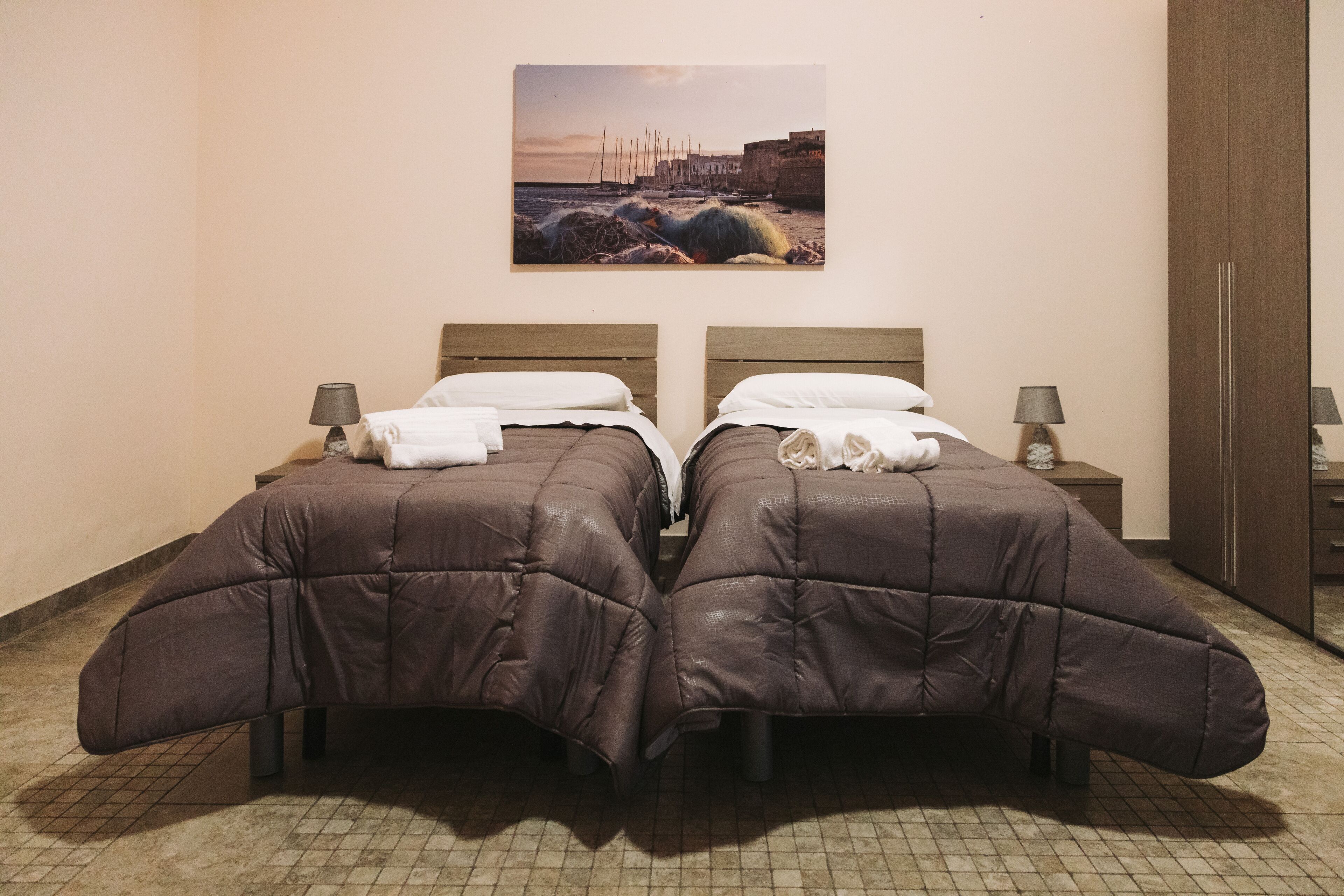 A double bed with a headboard, a bedside table with a lamp, and a painting of a coastal scene on the wall.