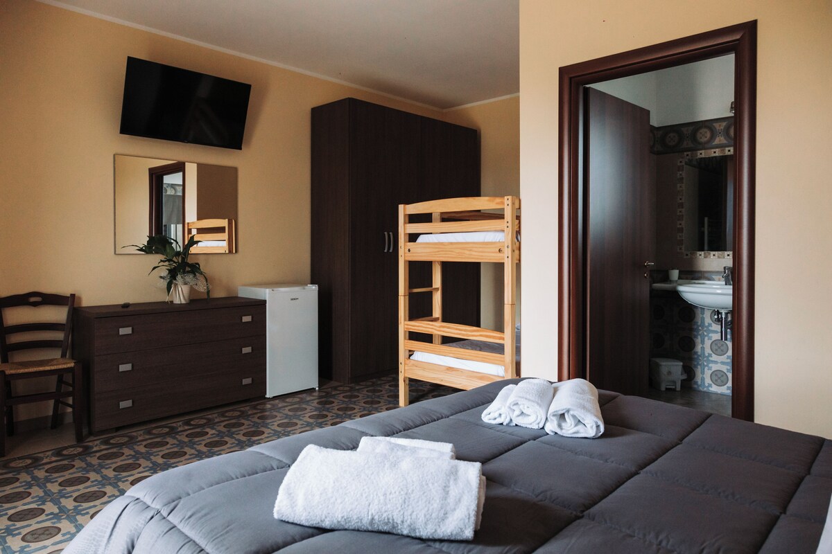 A hotel room with a bunk bed, a dresser, a television mounted on the wall, and a bathroom visible through an open door.