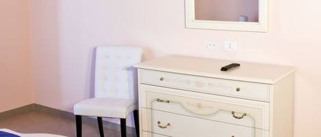 Un dormitorio con una cama, un tocador, una silla, una araña, un espejo y un televisor en la pared.
