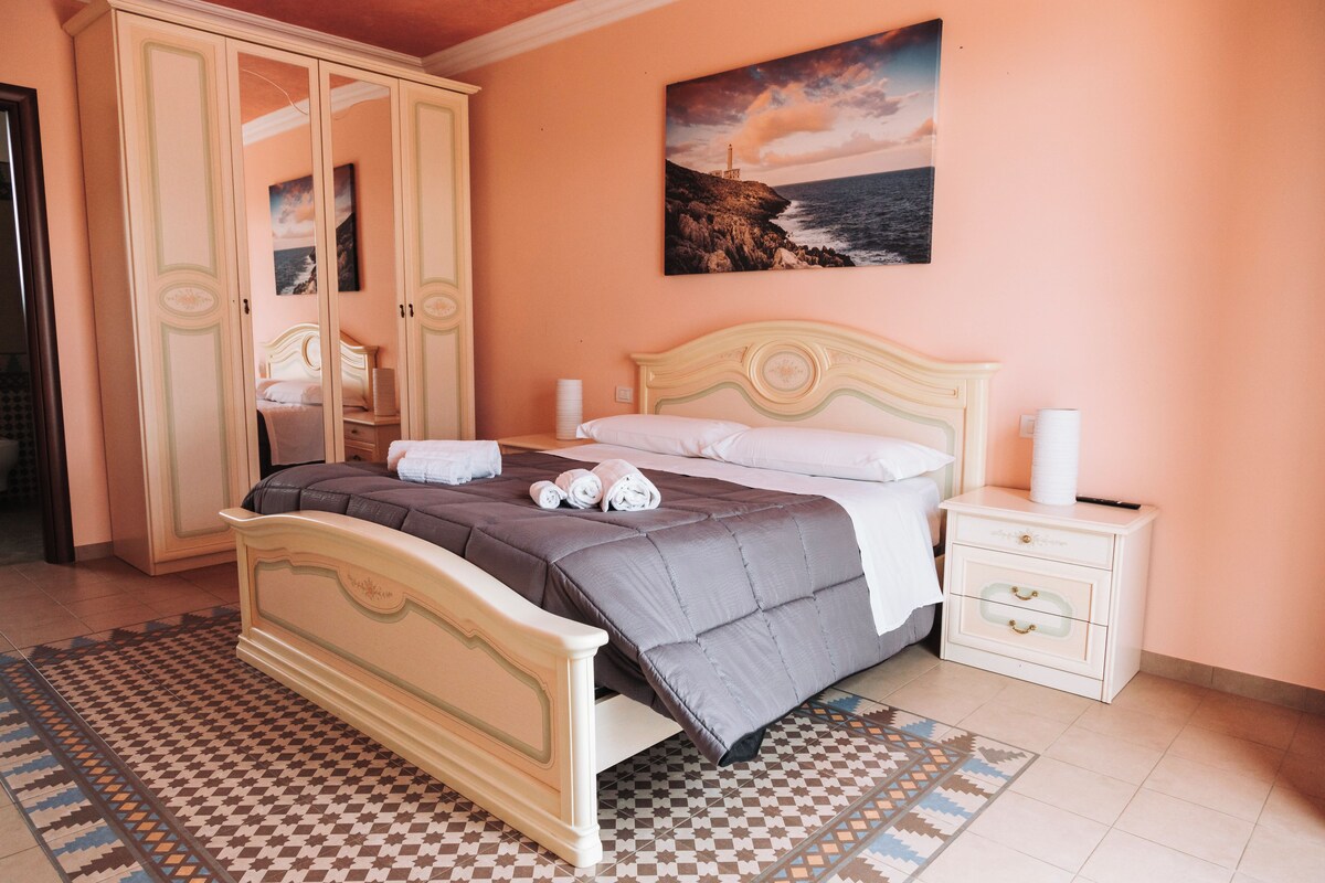 A bedroom with a bed, nightstand, wardrobe, and a painting of a lighthouse.