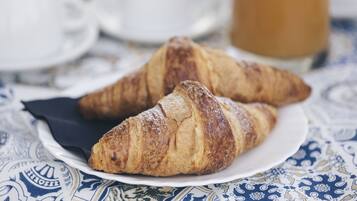 Zwei Croissants auf einem weißen Teller mit gemustertem Tischtuch.