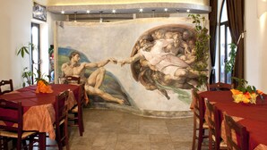 A dining area with a mural, wooden chairs, and tables covered with red tablecloths. - Agriturismo Paradiso (Parabita)