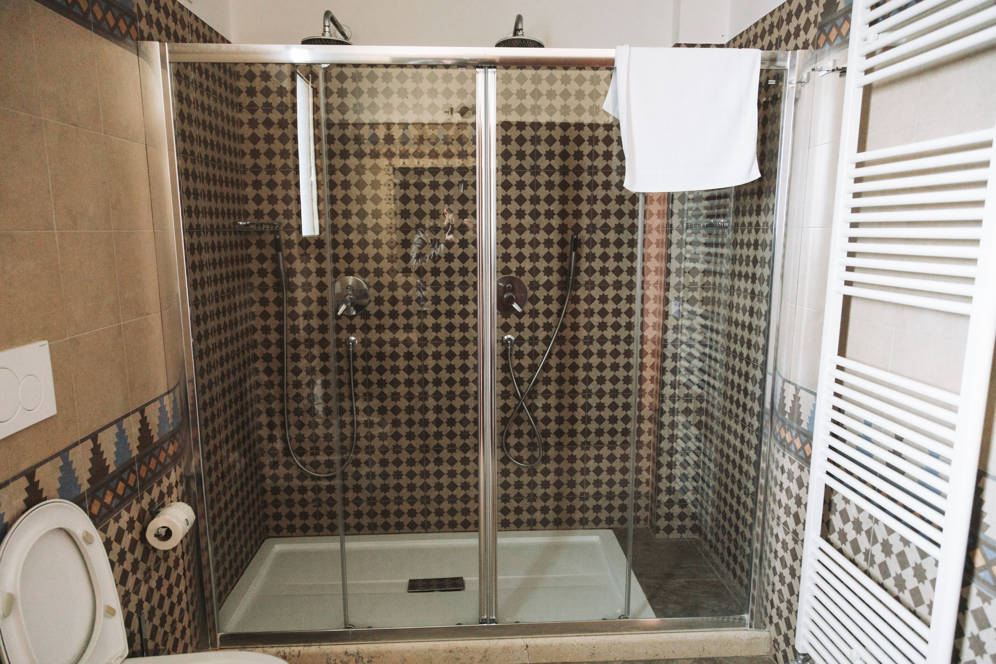 Una ducha con puerta de vidrio, una toalla colgada en la puerta y un muro con azulejos estampados.