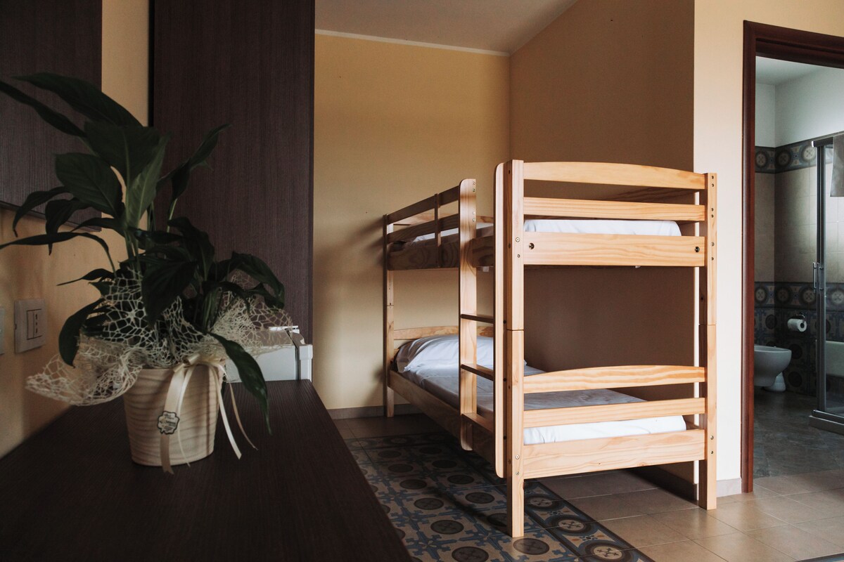 A room with a bunk bed, a potted plant, and a bathroom visible through an open door.