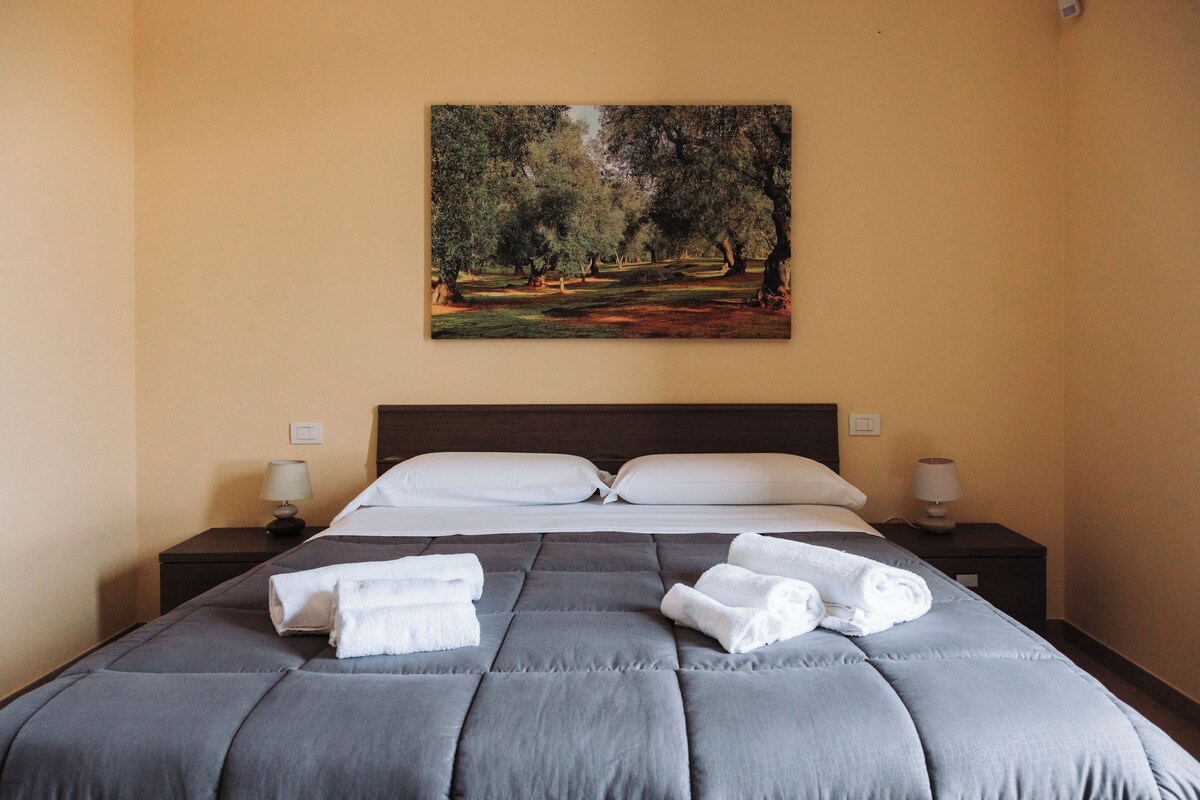 A hotel room with a large bed, two bedside tables with lamps, and a painting of a forest on the wall.