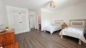 Habitación de hotel con dos camas, un aparador de madera, un escritorio con lámpara y una lámpara colgante.