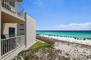 A beachfront hotel with a balcony overlooking a sandy beach with blue umbrellas. - Inlet Reef 307 3 Bedroom Condo by RedAwning (Destin)