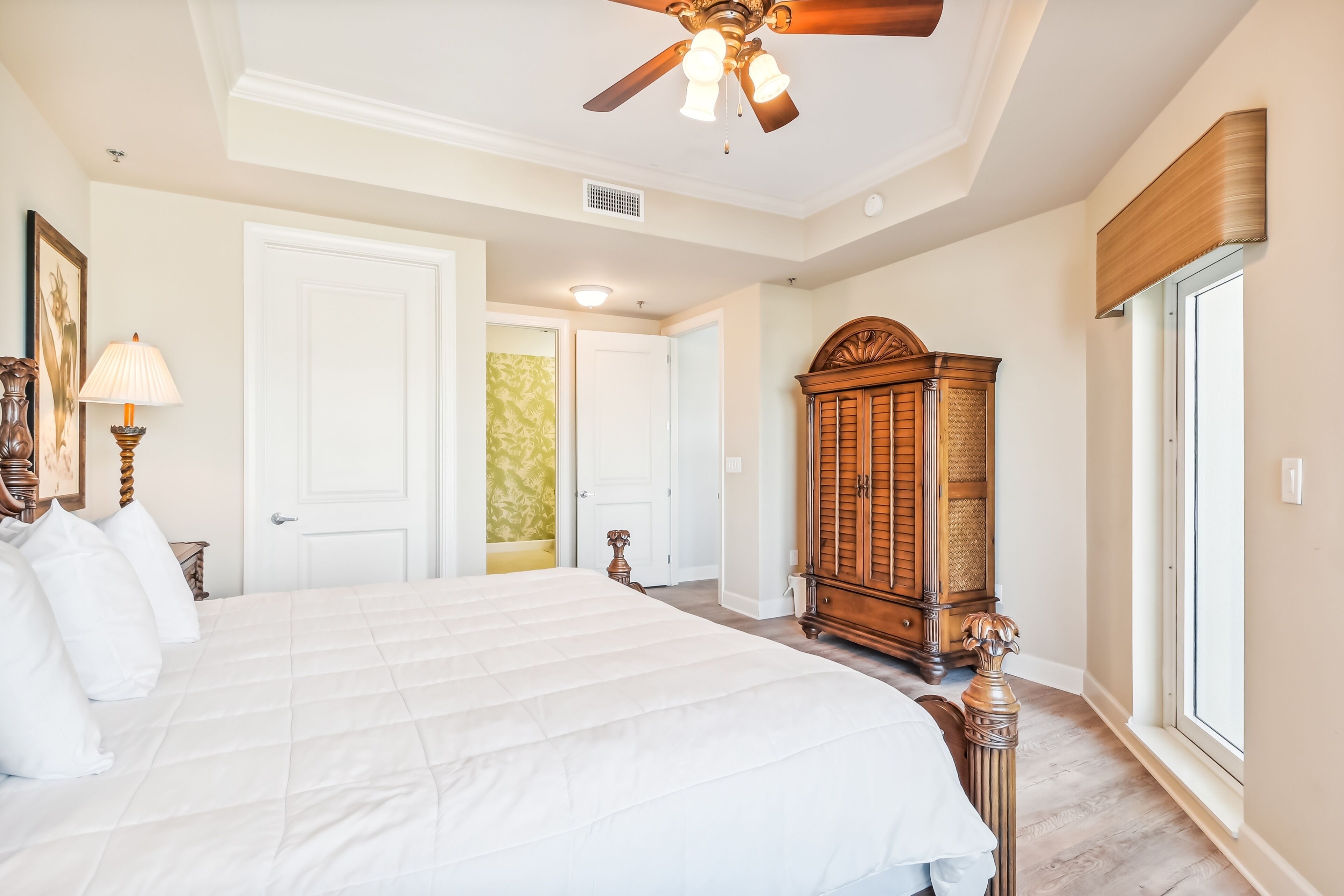 A spacious bedroom with a large bed, a ceiling fan, a wooden wardrobe, and a window.