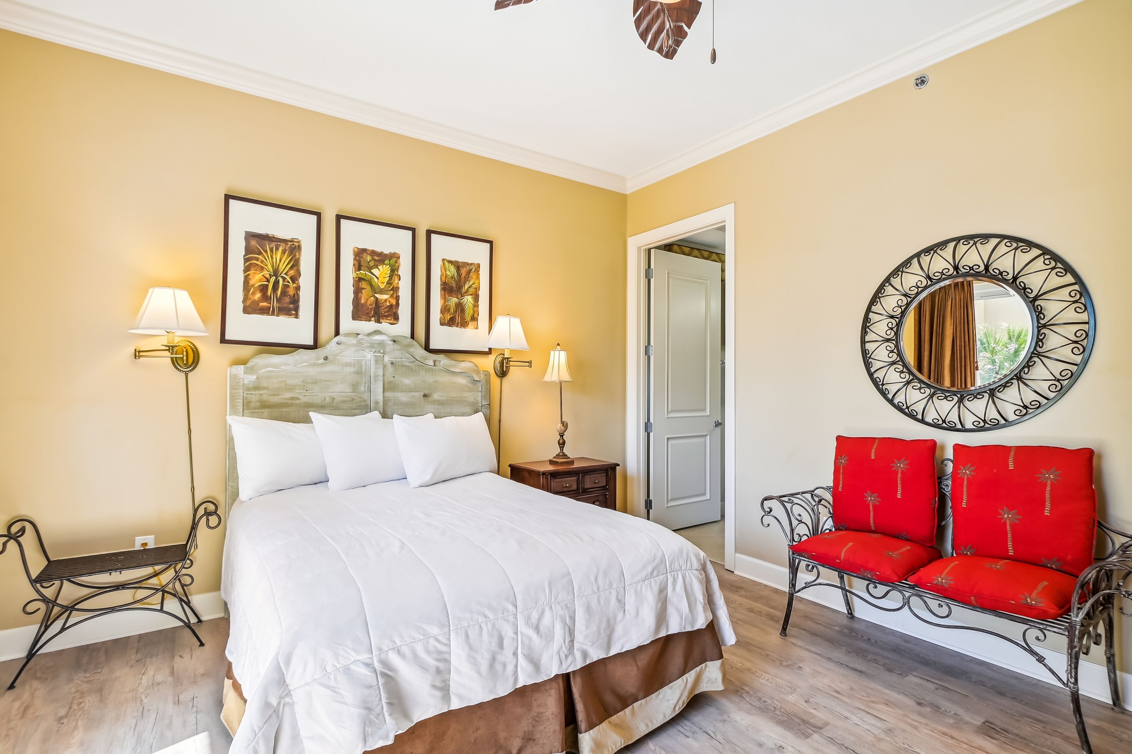 A bedroom with a large bed, two bedside tables with lamps, a red chair, and a mirror on the wall.