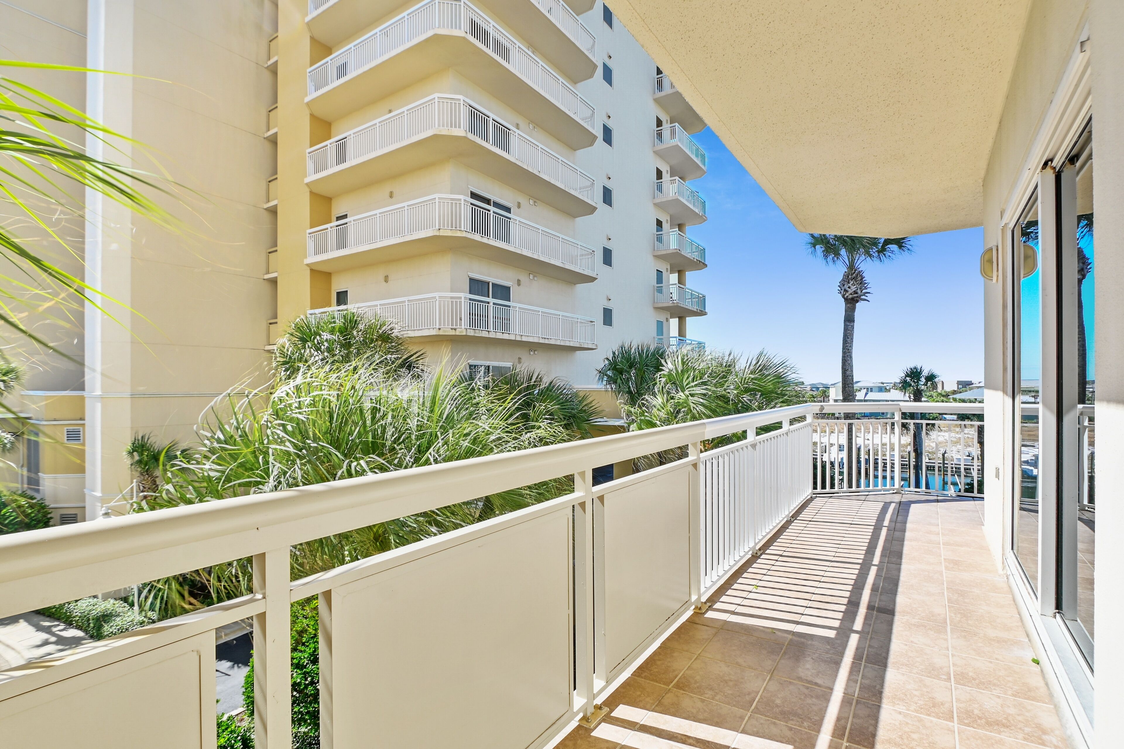 A balcony with a white railing, a tiled floor, and a view of a tall building with multiple balconies.