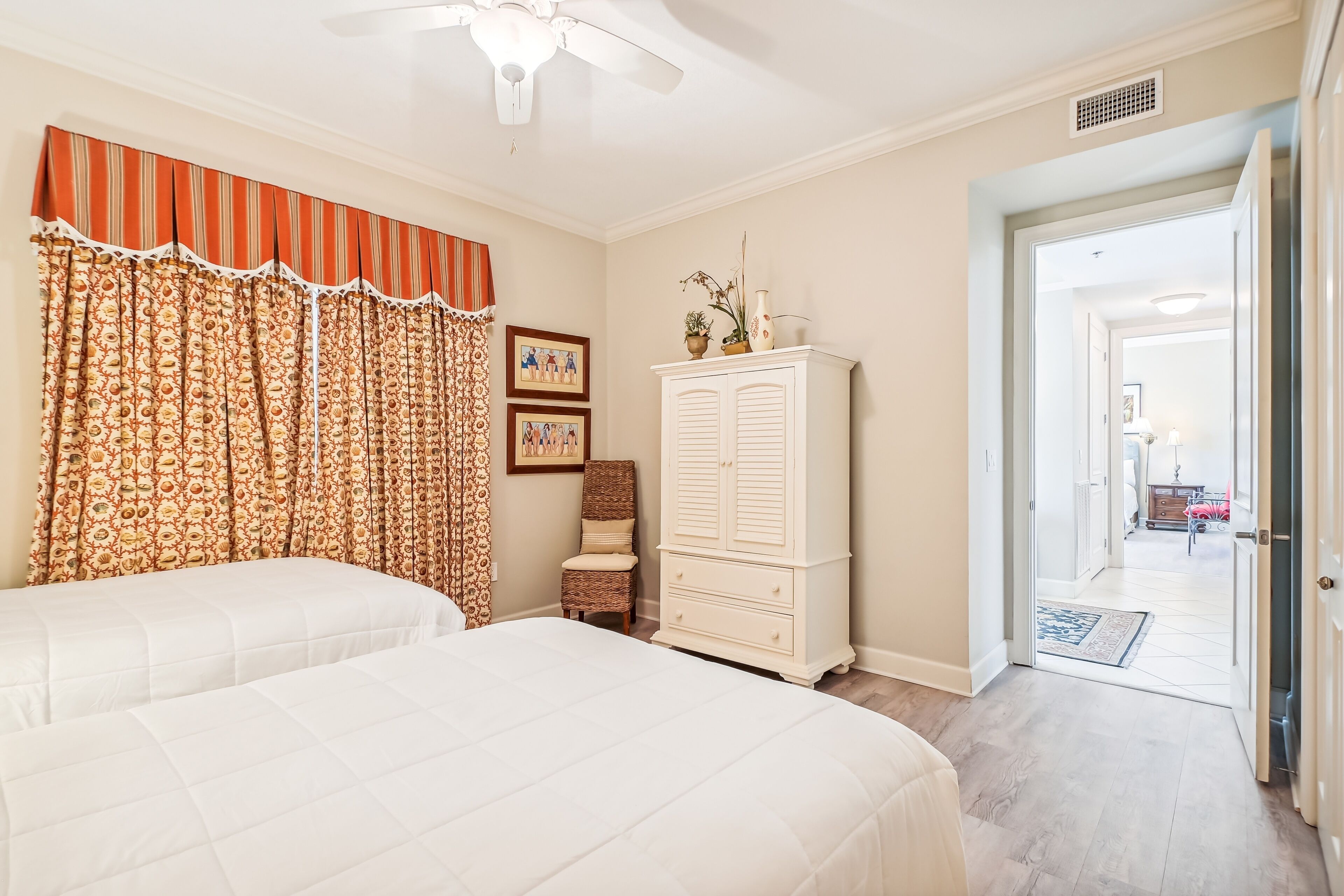 A bedroom with two beds, a wardrobe, a chair, and a door leading to another room.