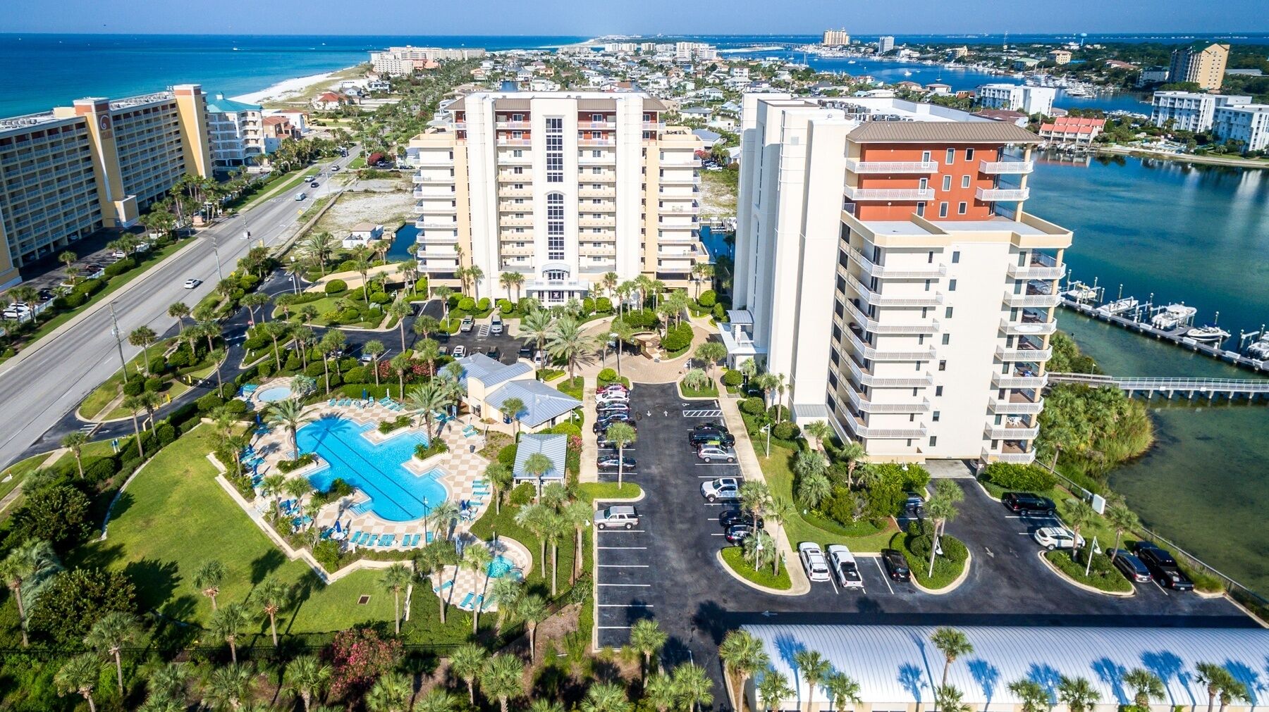 A high-rise hotel with a central pool, multiple parking levels, and a marina in the background.
