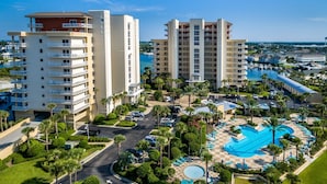 A high-rise hotel with multiple balconies, a central swimming pool, and a marina in the background.