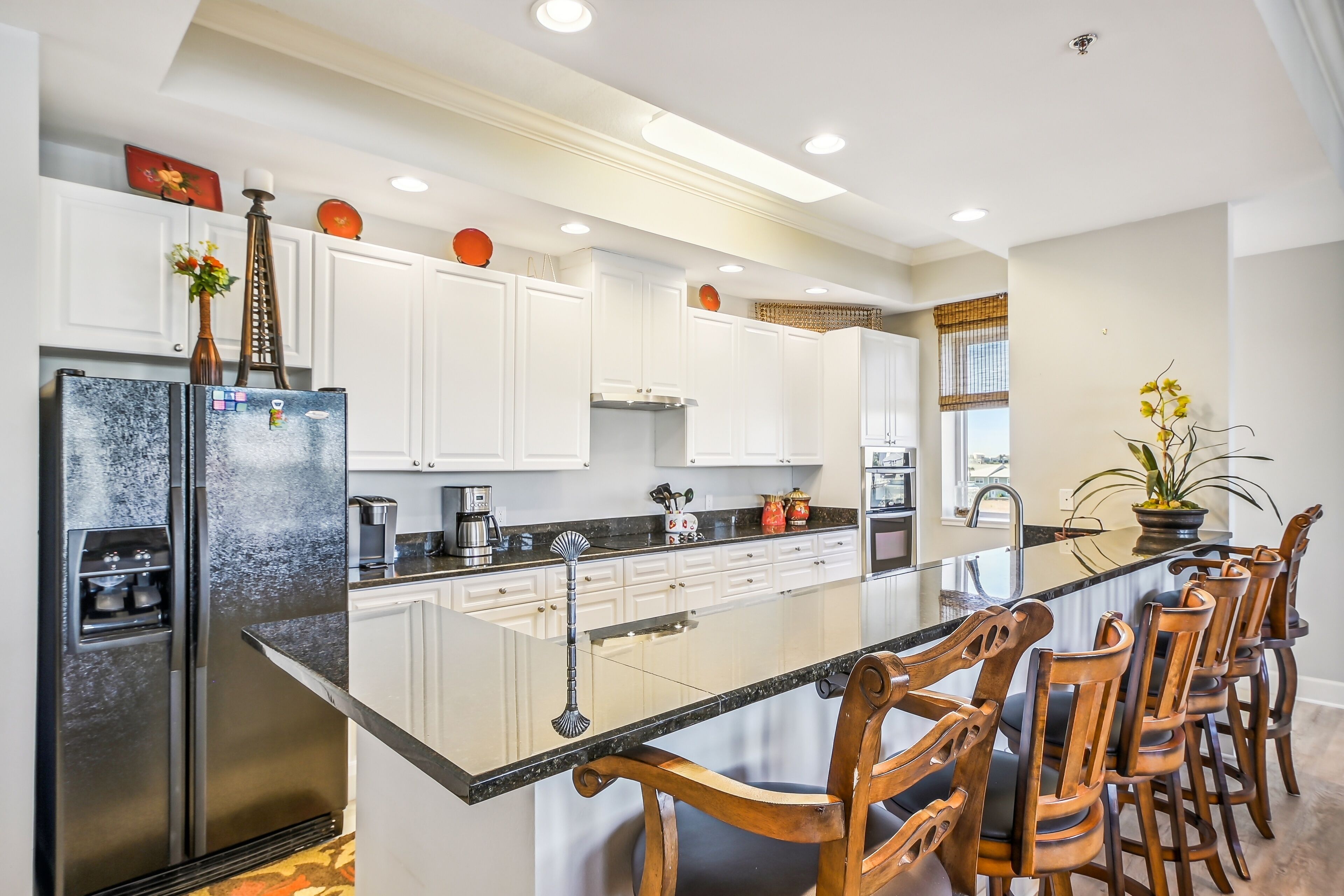 A modern kitchen with white cabinets, a stainless steel refrigerator, a black countertop, and wooden bar stools.