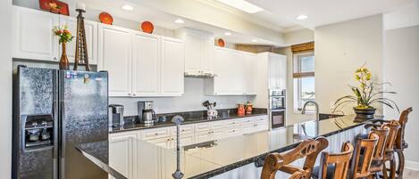 A modern kitchen with white cabinets, a stainless steel refrigerator, a black countertop, and wooden bar stools.