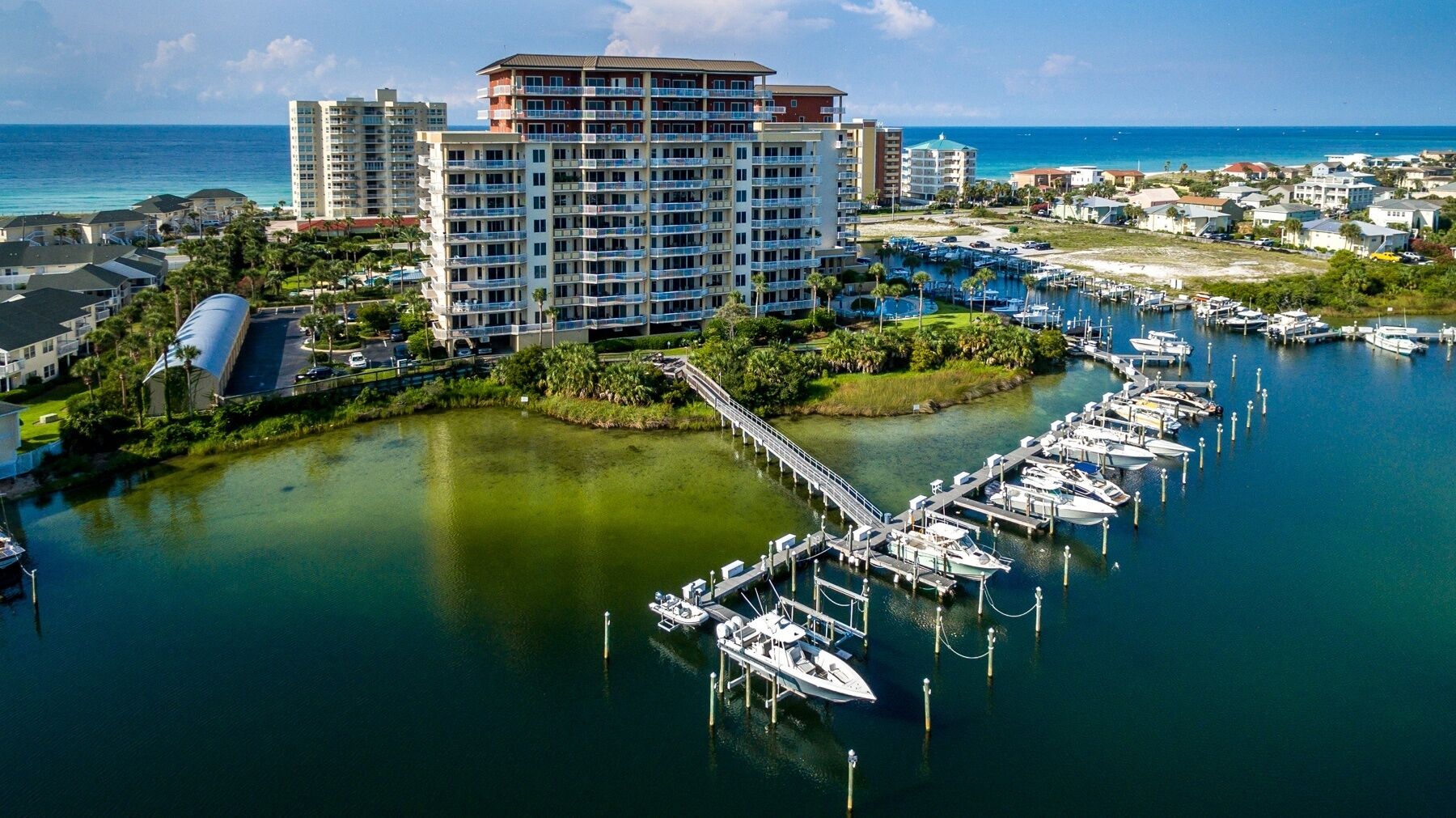 A marina with boats docked, a bridge connecting to a hotel, and a clear view of the ocean.