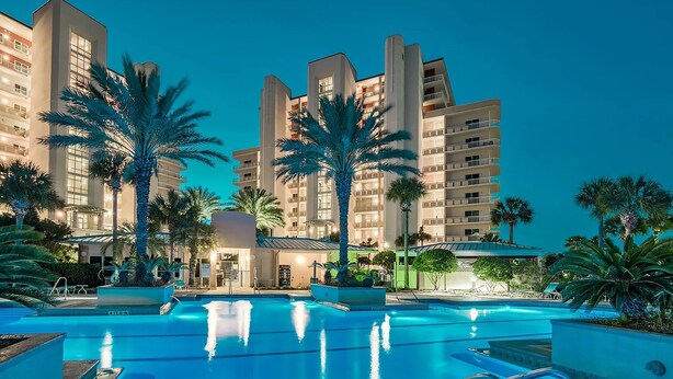 A hotel with a swimming pool, palm trees, and modern architecture.