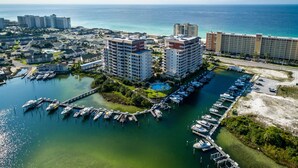 An aerial view of a marina with multiple boats docked, surrounded by high-rise hotels and a clear view of the ocean.