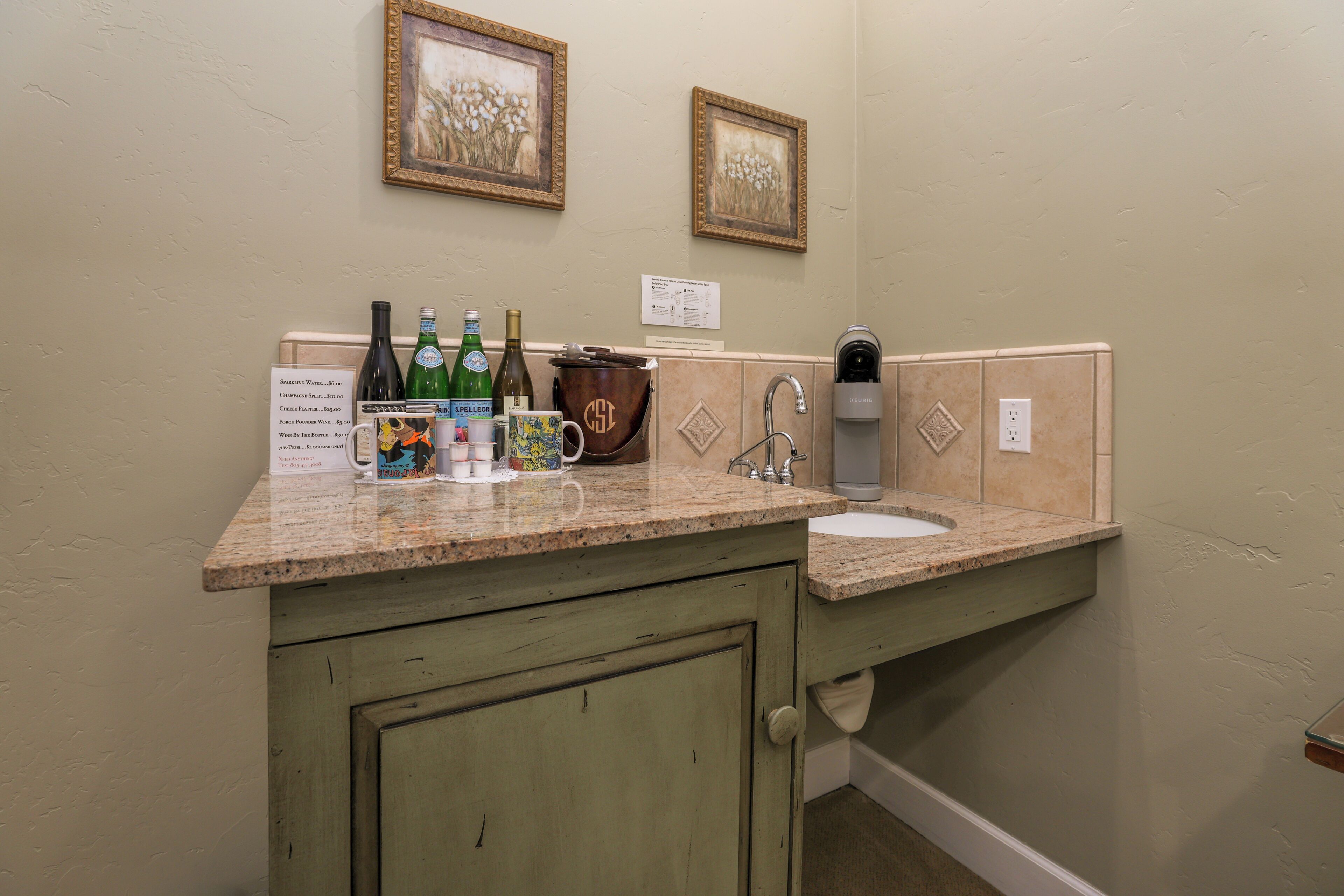 A bathroom with a granite countertop, a sink, a coffee maker, and two framed pictures on the wall.