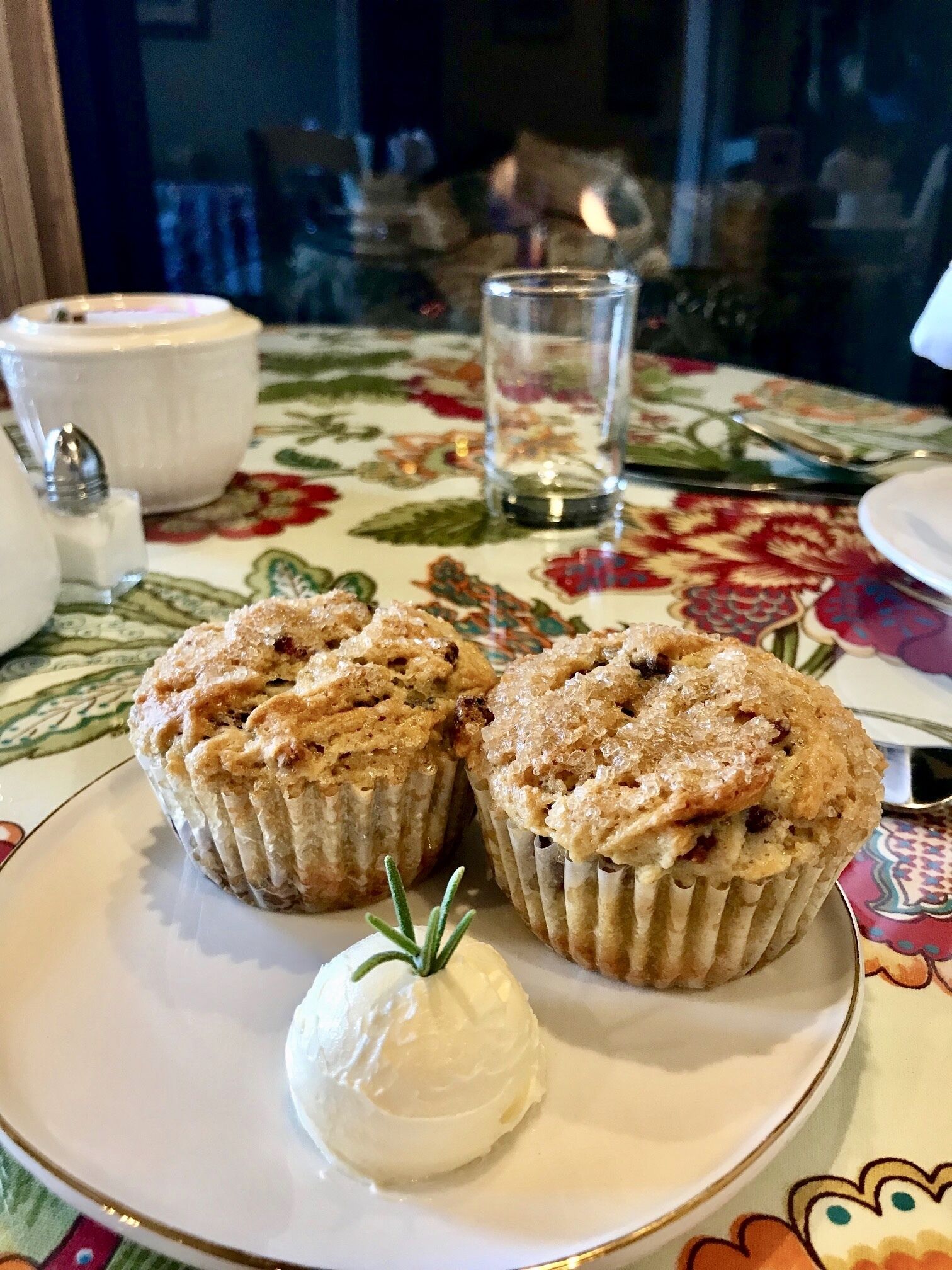 Un plato con dos muffins y una bola de helado sobre una mesa con mantel floreado.