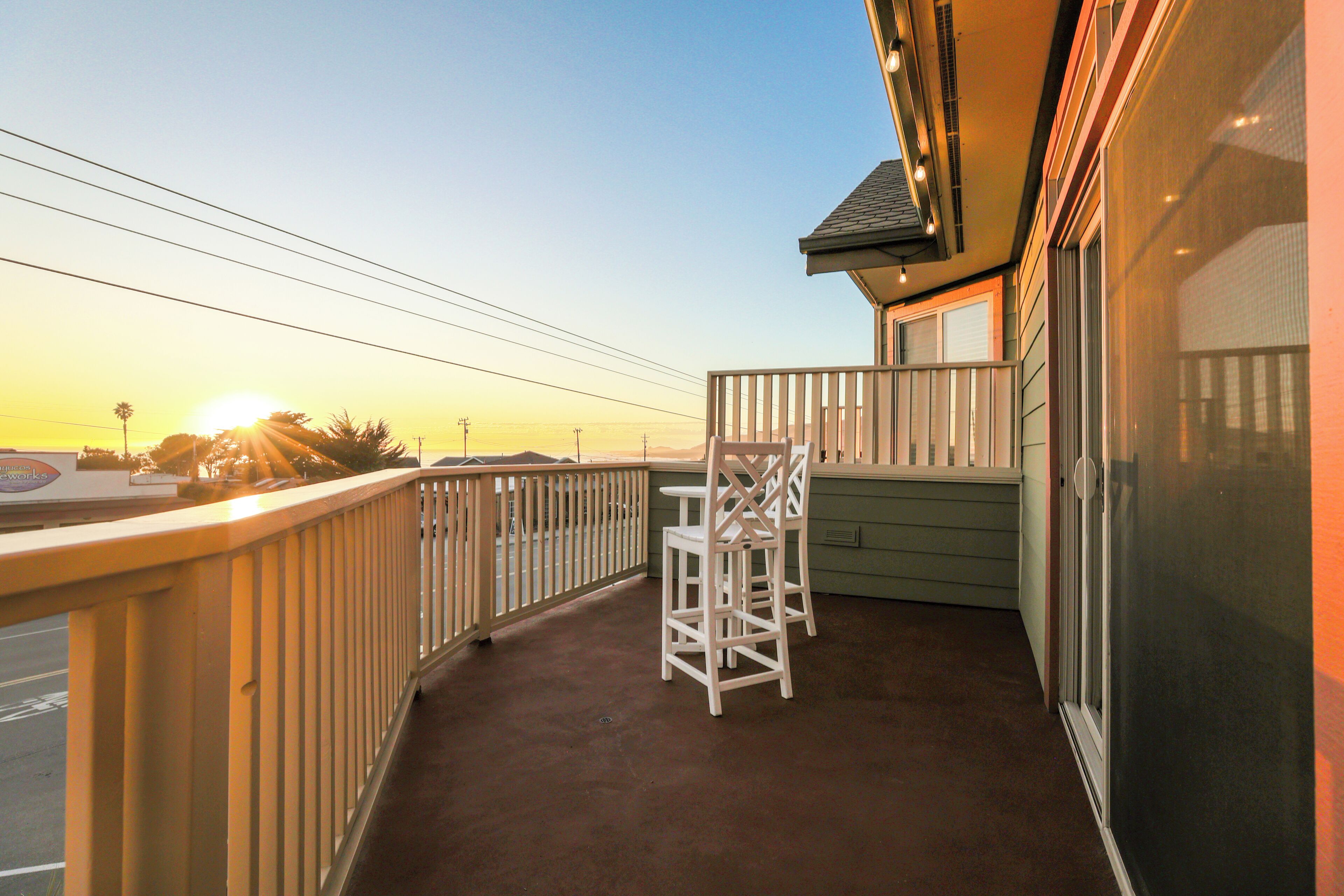 A balcony with a view of the sunset, a white chair, and a green wall.