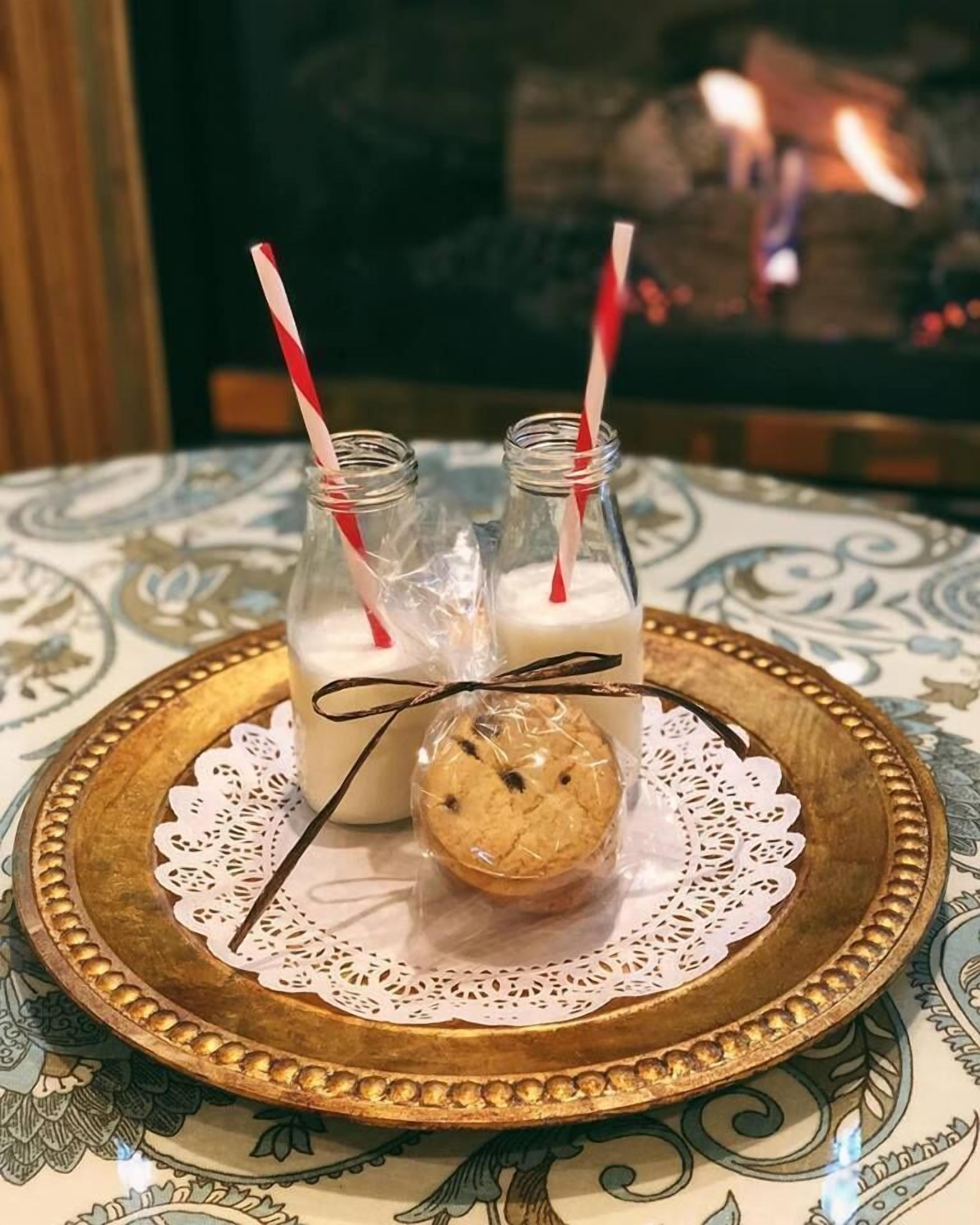 A tray with two milk bottles and a cookie on a tablecloth with a lace doily.