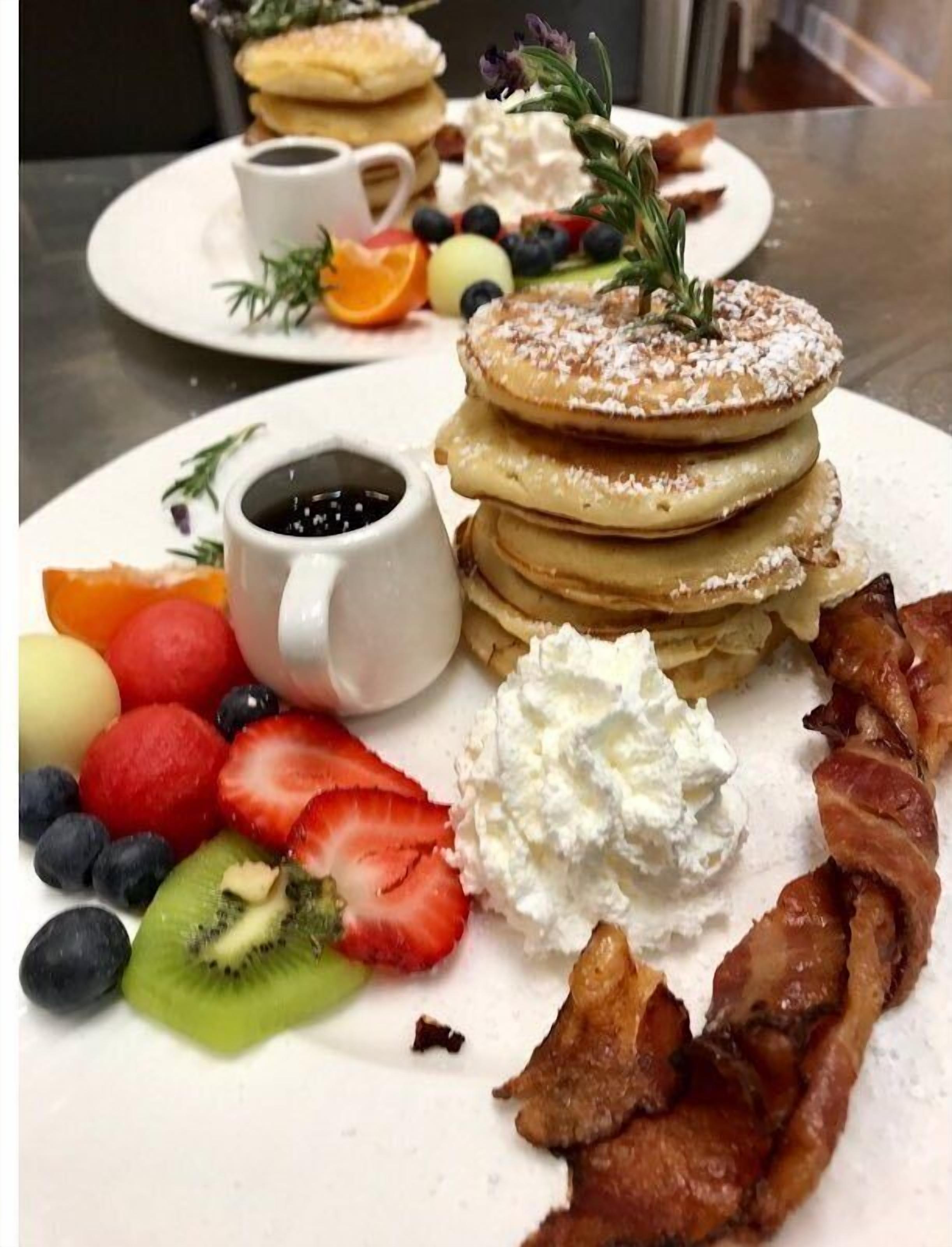A breakfast plate with pancakes, bacon, whipped cream, and fresh fruit.