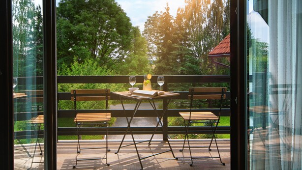 A balcony with a table set for two, a bench, and a view of a lush green landscape. - Lagom Apartments (Rakovica)