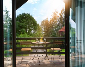 A balcony with a table set for two, a bench, and a view of a lush green landscape. - Lagom Apartments (Rakovica)