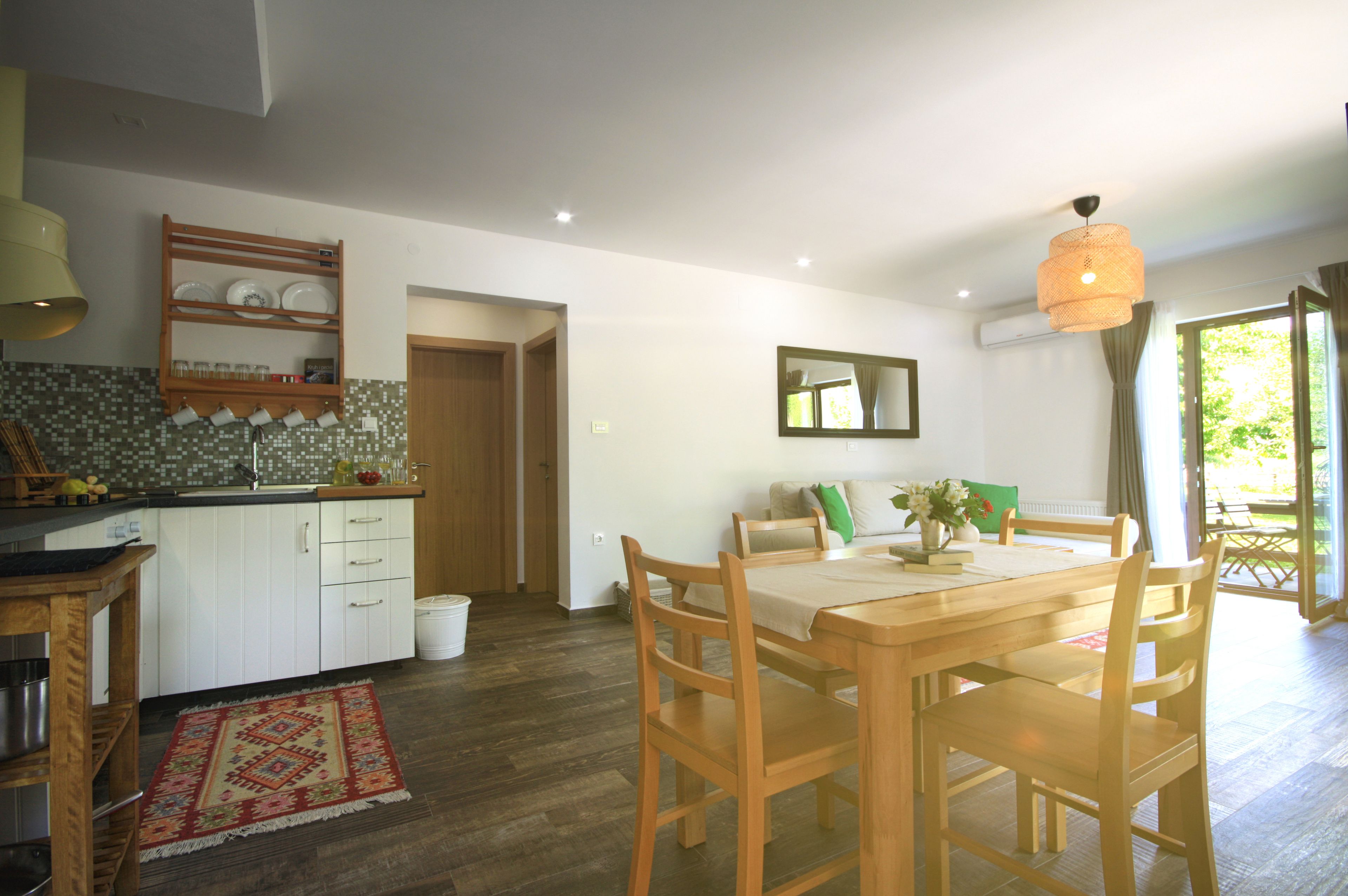 A modern kitchen with white cabinets, a wooden dining table, and a red patterned rug.