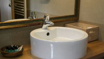 Un baño con un lavamanos blanco, un cuenco de madera con artículos de aseo y un espejo con marco decorativo.