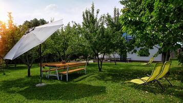 A grassy outdoor area with a wooden bench, a yellow lawn chair, and a white umbrella.