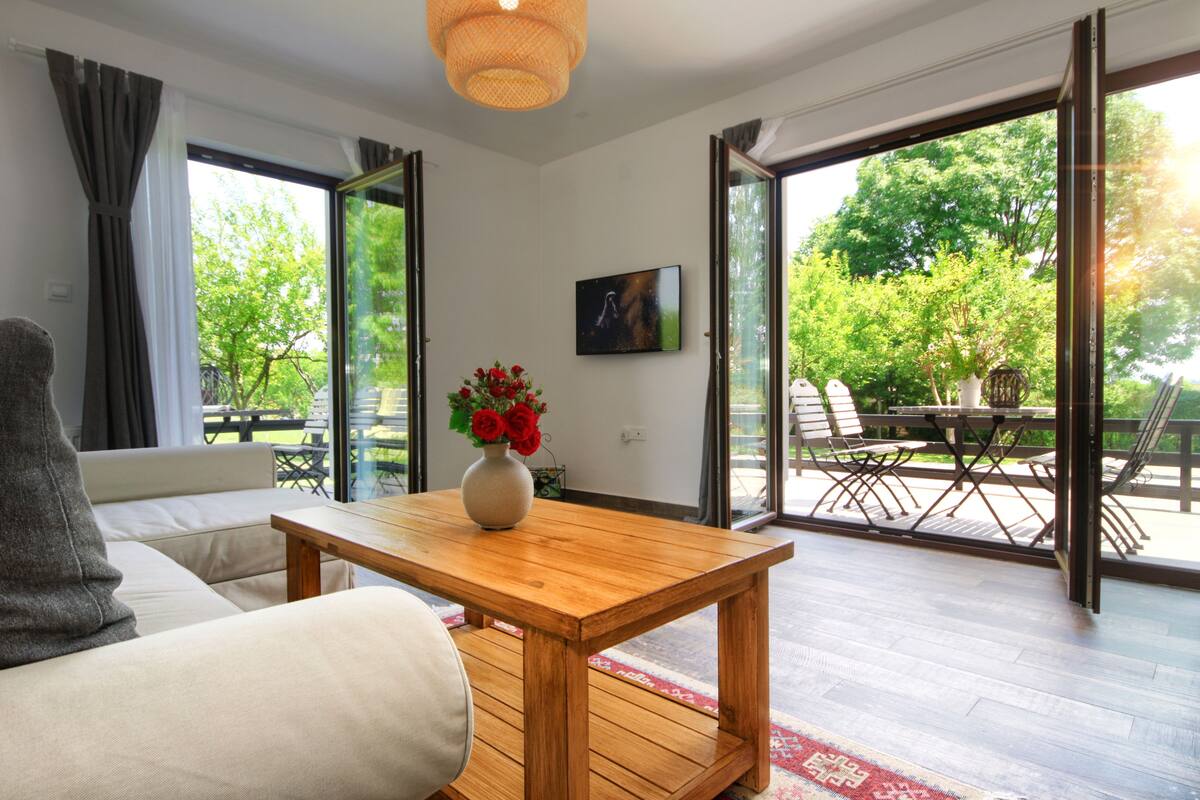 A modern living room with a sofa, a wooden coffee table with a vase of flowers, and a television on the wall.