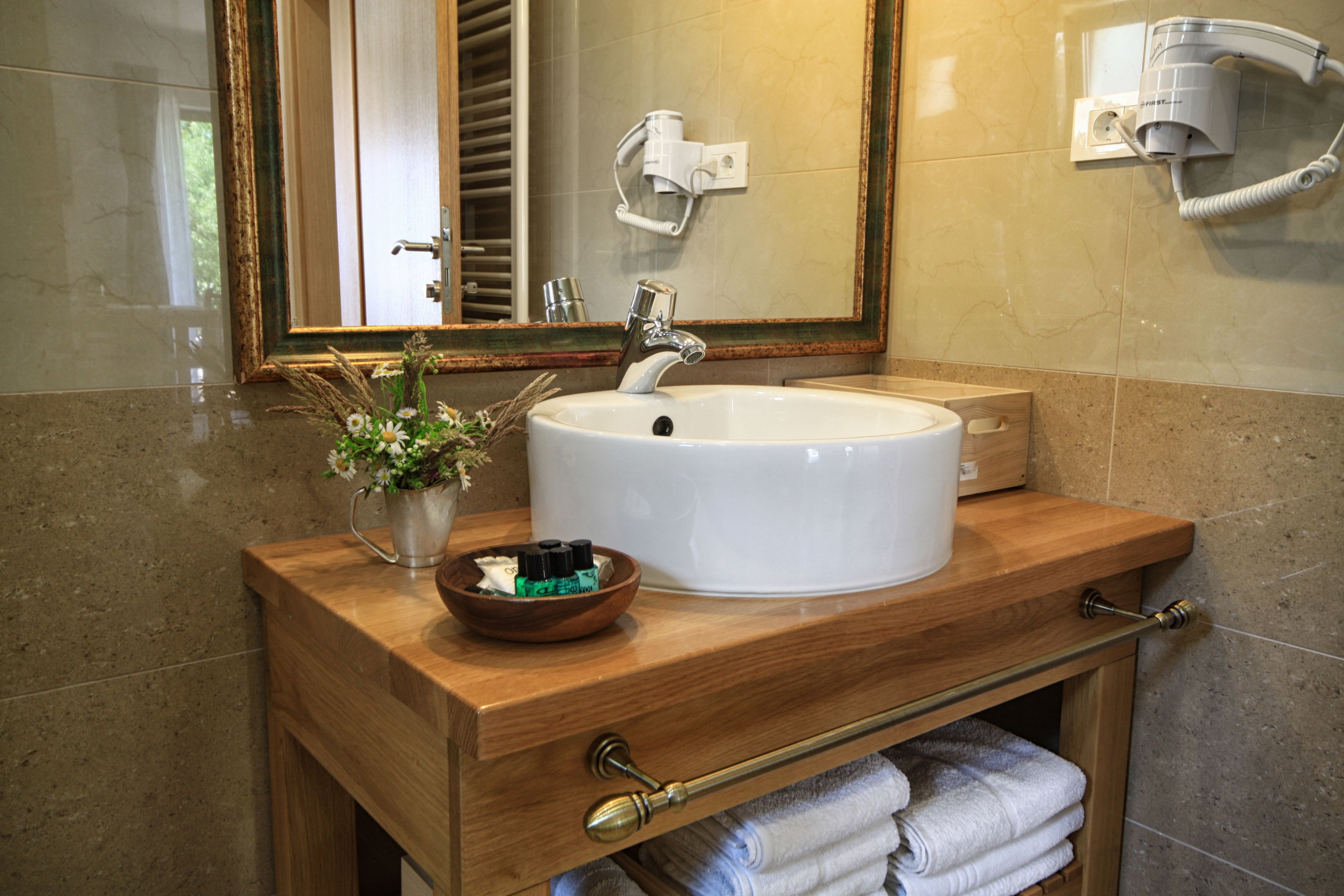 A bathroom with a wooden vanity, a white sink, a mirror, a towel rack, and a hairdryer mounted on the wall.