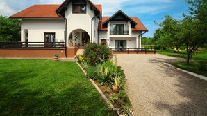 A two-story house with a red-tiled roof, a front porch, and a landscaped garden with a gravel driveway. - Lagom Apartments (Rakovica)